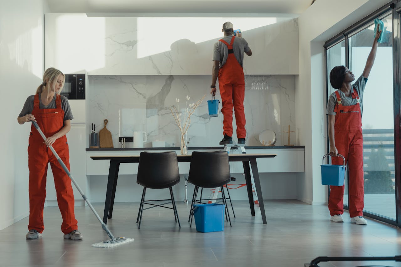 hero-img-01 Group of cleaners in red uniforms mopping and wiping glass in a modern dining room.